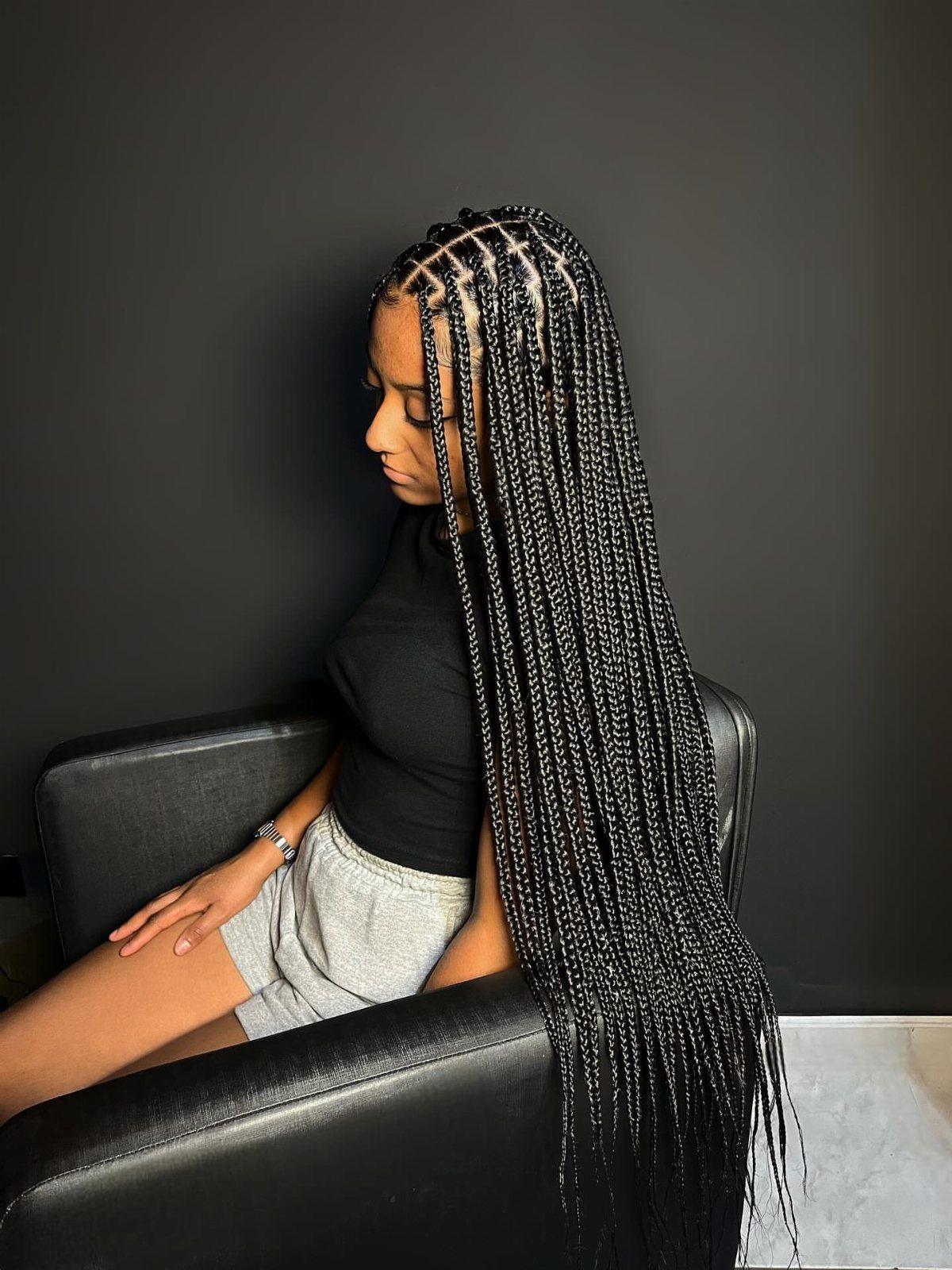 Woman with long black box braids sitting in a black leather chair