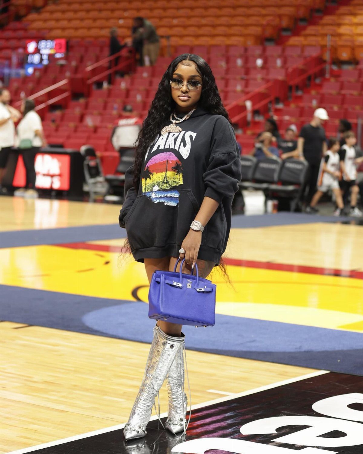Woman in black graphic hoodie and silver boots posing on a basketball court.