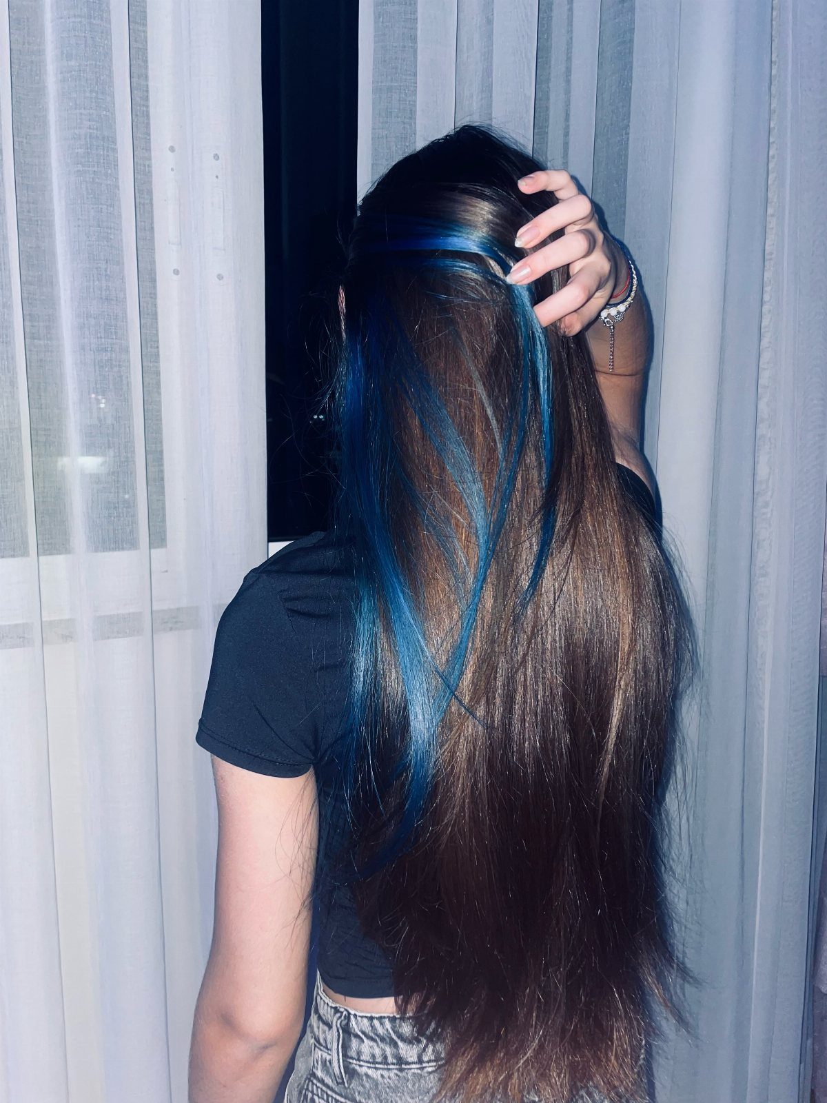 Long brown hair with vibrant blue highlights seen from behind against white curtains.