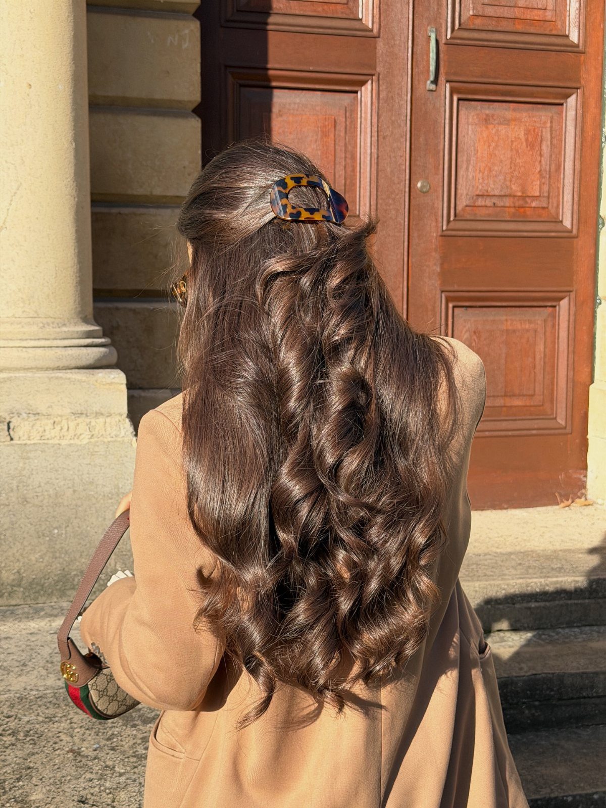 Long wavy brown hair partially held up with a tortoiseshell clip from behind.