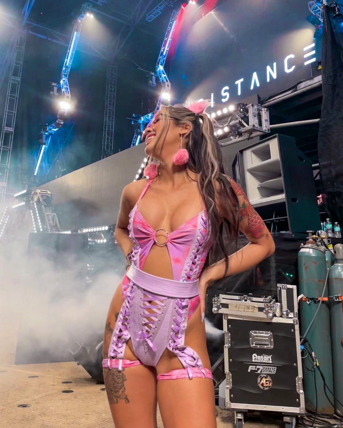 Woman in a pink metallic cutout bodysuit posing on a concert stage with lighting.