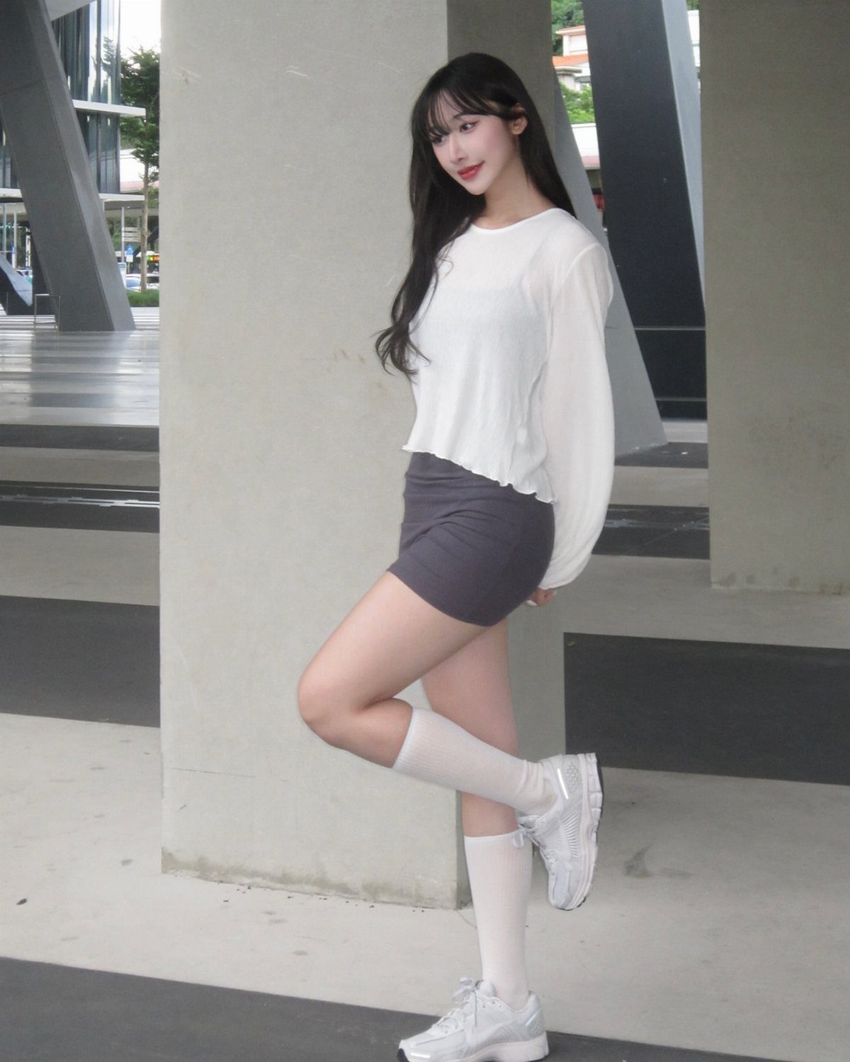 Woman wearing a white top, short gray skirt, white knee-high socks and white sneakers.