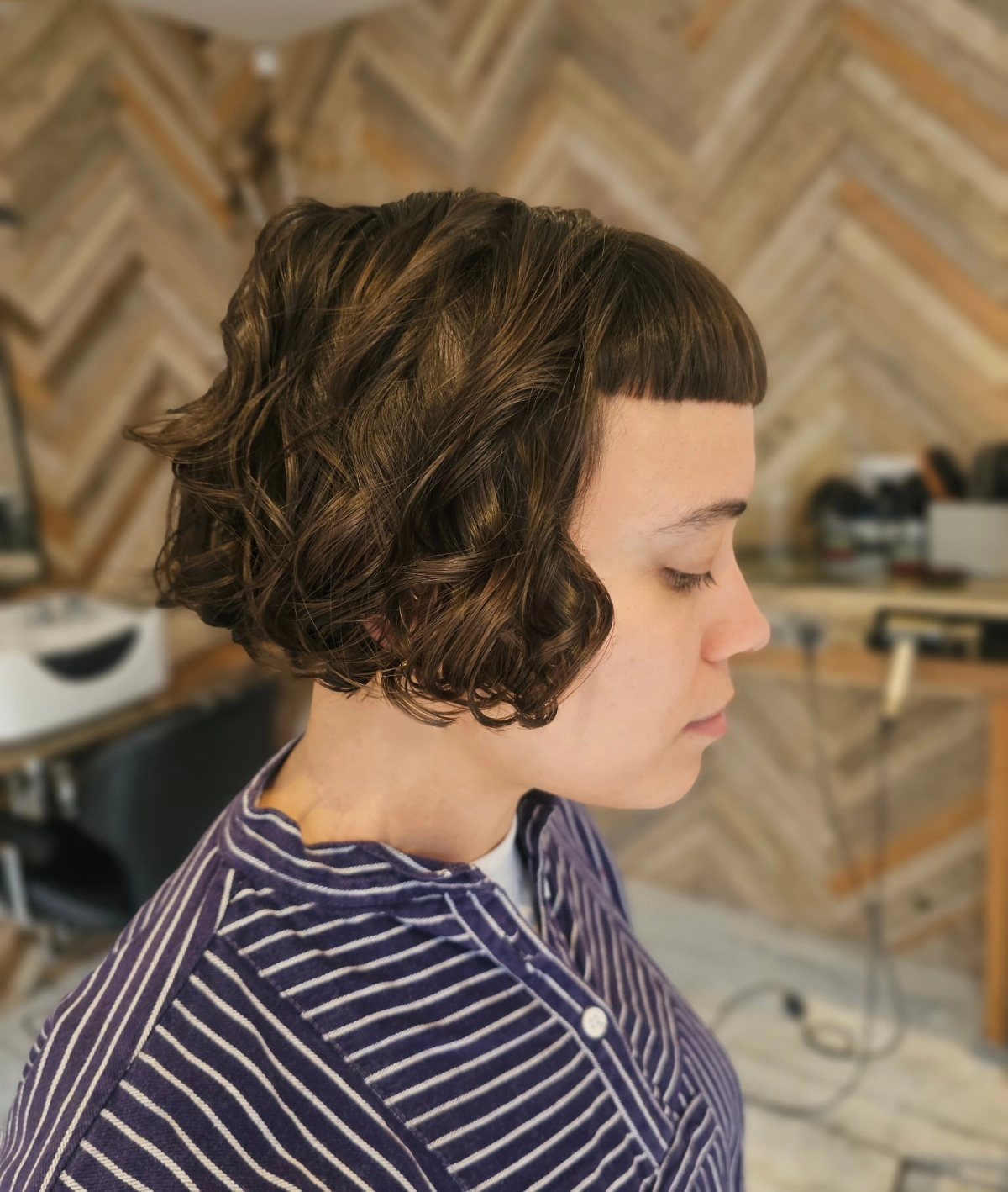 Person with a curly brown bob and short micro bangs against a chevron wall.