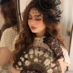 Woman wearing a black fascinator hat with a dotted veil and lace gloves.