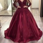 Burgundy satin ball gown with long sleeves and beaded embroidery on a person.