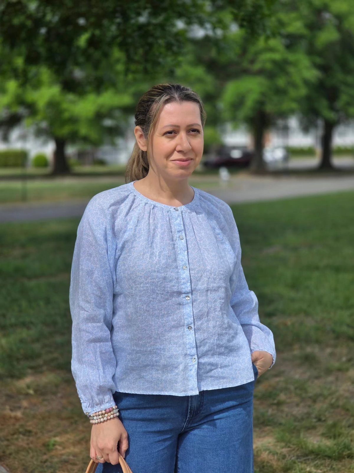 Woman wearing a light blue button-up blouse and blue jeans in a park.