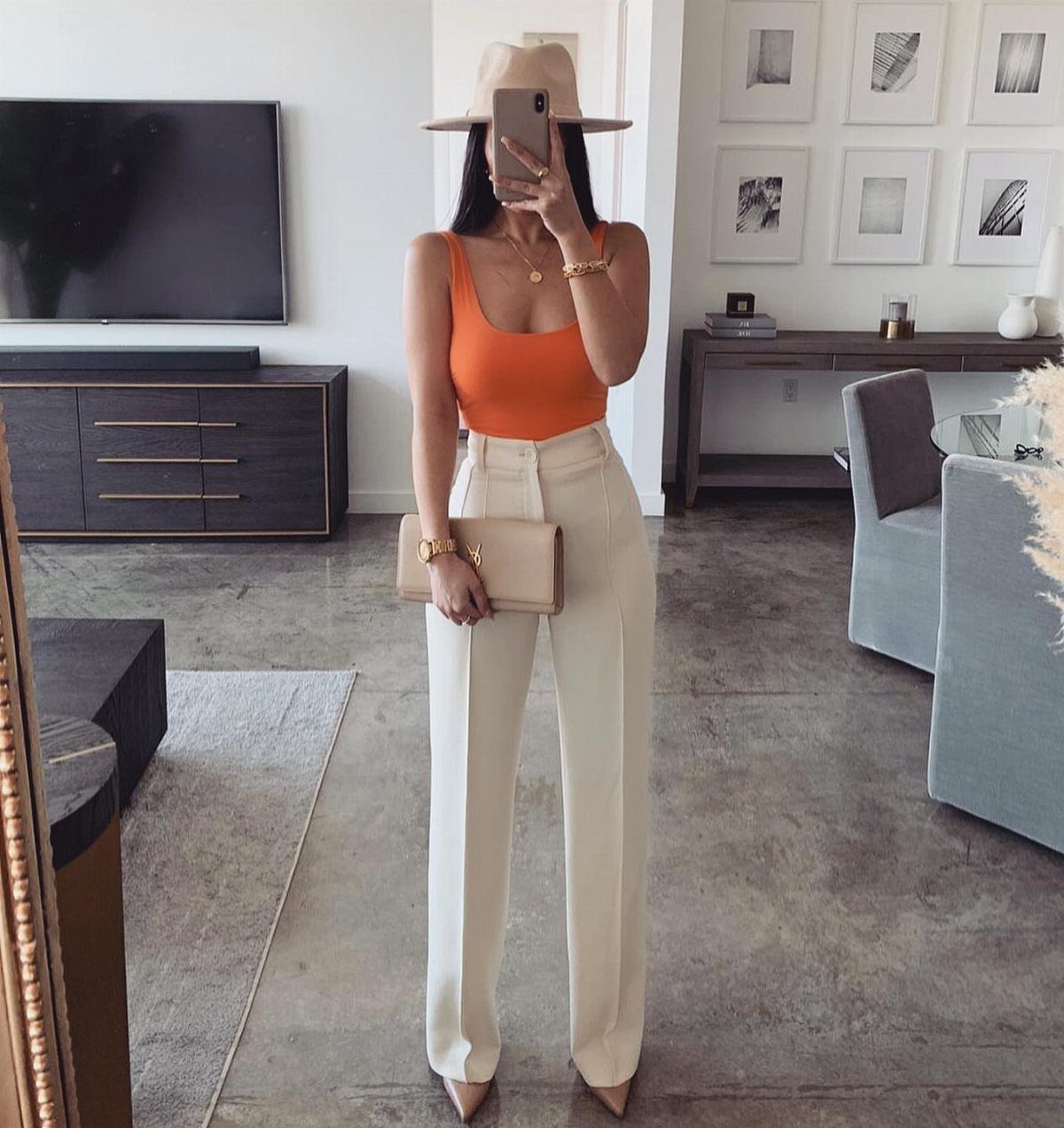 Woman in orange tank top and off-white linen pants wearing a tan hat.